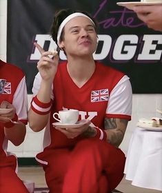 two men sitting on the floor eating cake and drinking tea while one man is holding a cell phone to his ear