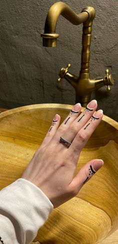 a woman's hand with tattoos on her fingers in front of a wooden bowl