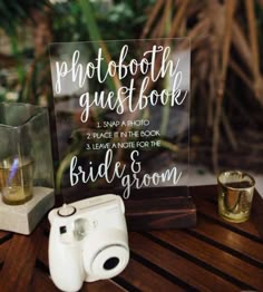 a wooden table topped with a sign next to a couple's wedding rings and binoculars