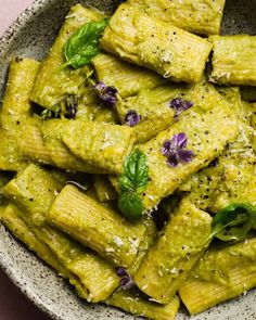 a white bowl filled with pasta covered in pesto sauce and garnished with purple flowers