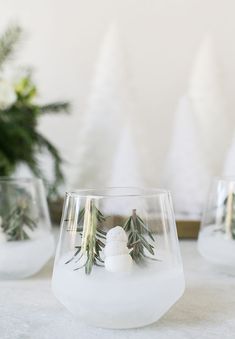 three wine glasses sitting on top of a table covered in snow and greenery next to evergreen cones