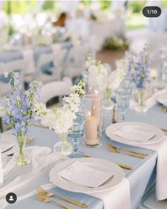 the table is set with white and blue flowers in vases, silverware, and candles