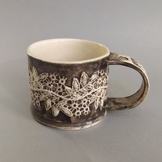 a white and black coffee cup with lace on the edge sitting on a gray surface