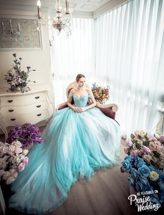 a woman in a blue dress sitting on a chair next to flowers and a chandelier