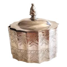 an old silver box with a lid on it's side and a small figure in the top