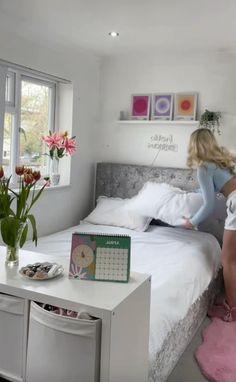 a woman sitting on top of a bed next to a table with flowers in it