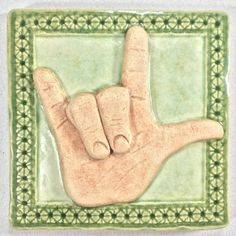 a green and white tile with a hand holding the peace sign on it's side