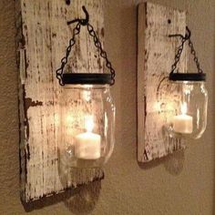 two mason jars are hanging on the wall with candles in them and one is holding a lit candle