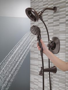 a person is holding the shower head and spraying it with their hands while standing in front of a tiled wall