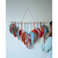 a woman is looking at an art piece hanging on the wall with red, white and blue feathers