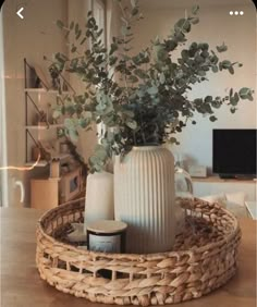 a wicker basket with vases and greenery in it sitting on a table