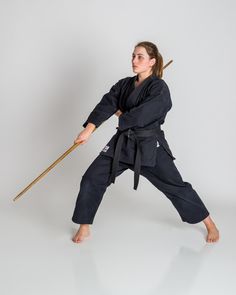 a woman in black karate outfit holding a wooden stick and standing on one leg with both hands