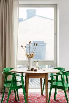 a dining room table with green chairs and a potted plant in the window sill