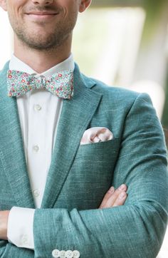 a man wearing a green suit and bow tie with his arms crossed in front of him