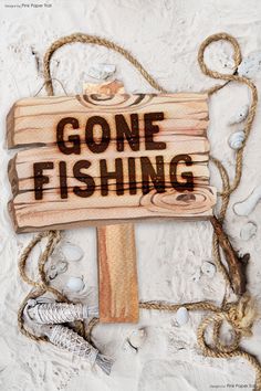 a wooden sign that says gone fishing hanging from a rope on top of the sand