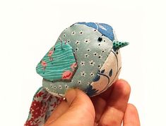 a hand holding a small blue bird with red and white flowers on it's head