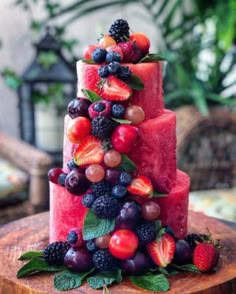 a watermelon cake with berries and cherries on the top is sitting on a wooden platter