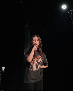 a woman standing in front of a microphone with her hand up to her mouth while singing