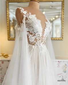 the back of a wedding dress with white lace and flowers on it, in front of a mirror