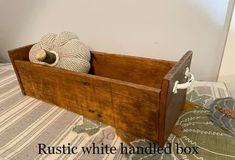 a wooden box sitting on top of a bed with two balls in it and the words rustic white handled box below