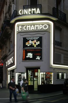 people walking on the street in front of a movie theater at night with neon lights