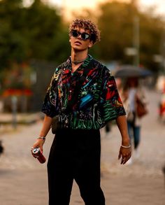 a man walking down the street with an umbrella in hand and sunglasses on his head