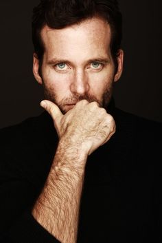 a black and white photo of a man with his hand on his chin looking at the camera