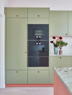 a kitchen with green cabinets and white counter tops, flowers in a vase on the island