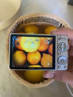 a person holding a camera in front of a bowl of oranges