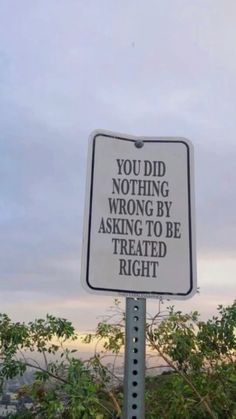 a sign that is on top of a pole in the grass with trees behind it