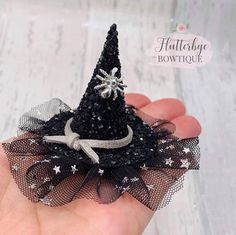 a hand holding a tiny black hat with silver stars on it and a ribbon around the top