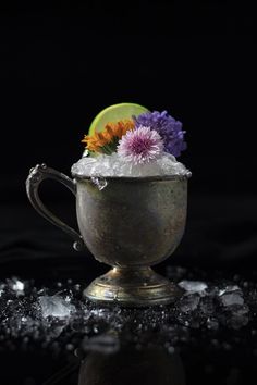 a silver cup filled with ice and flowers on top of a black table next to a slice of lime