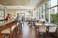 people are sitting at tables in a restaurant with large windows and wood flooring on the walls