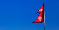 a red and white flag flying in the wind on top of a building with a blue sky behind it