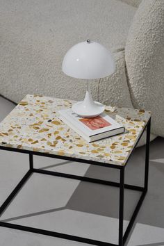 a white lamp sitting on top of a table next to a couch with a book