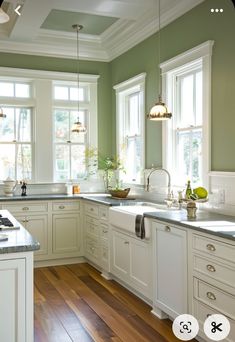 a kitchen with green walls and white cabinets, wood flooring and an island in the middle