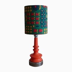 an orange table lamp with a green and red lampshade on the base, against a white background