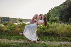 a man and woman kissing in front of a body of water with trees behind them