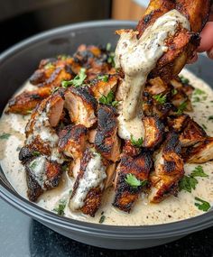 a person is dipping sauce on chicken wings in a bowl filled with ranch dressing and garnished with parsley