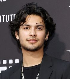 a young man in a black suit and necklace