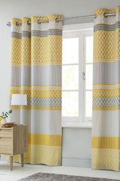 a yellow and white curtain hanging in front of a window next to a wooden dresser