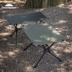 a small black table sitting on top of a gravel covered ground next to a forest