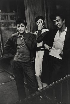 three young men are standing on the steps outside an apartment building, one is holding his hand up to his face