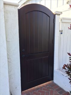 a brown wooden door sitting next to a white wall and red brick floored walkway