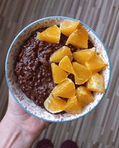 a person holding a bowl of food with oranges on the top and beans in it