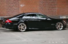 a black car parked in front of a brick building with white rims and chrome wheels