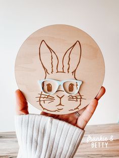 a person holding up a wooden cutout of a rabbit with glasses on it's face