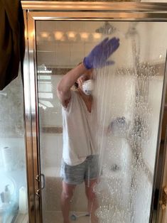 a man standing in front of a shower with blue gloves on his head and arms