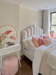 a white bed sitting next to a window with pink pillows and blankets on top of it