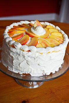 a cake with white frosting and sliced peaches on top is sitting on a glass plate